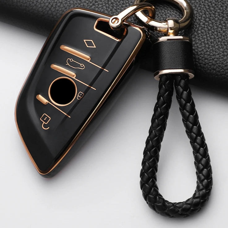 Black car key fob with gold accents and braided black leather strap on a white background